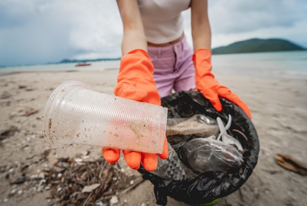 Una volontaria ecologista femminile pulisce la spiaggia in riva al mare da plastica e altri rifiuti