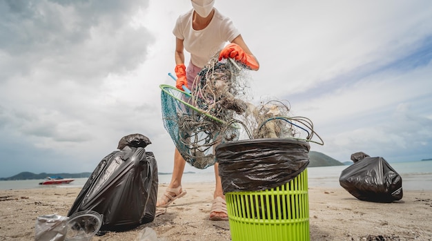 Una volontaria ecologista femminile pulisce la spiaggia in riva al mare da plastica e altri rifiuti