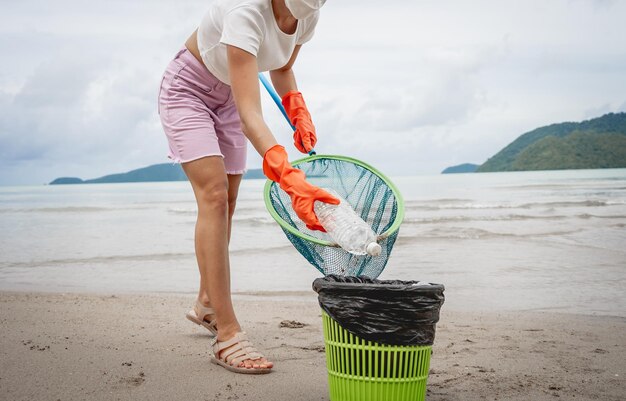 Una volontaria ecologista femminile pulisce la spiaggia in riva al mare da plastica e altri rifiuti