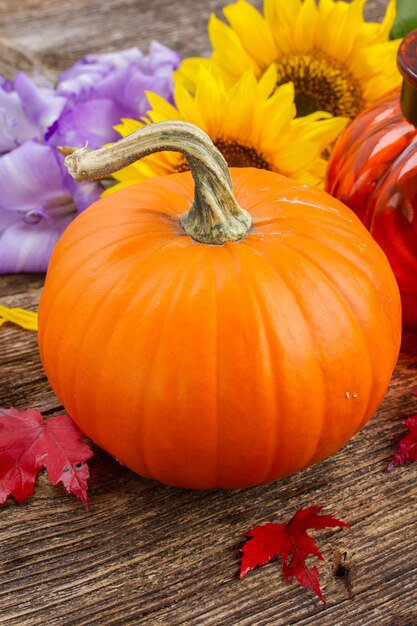 Una zucca arancione con fiori e foglie autunnali su un tavolo strutturato in legno