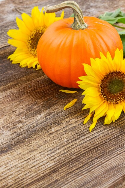 Una zucca arancione con girasoli su un tavolo strutturato in legno