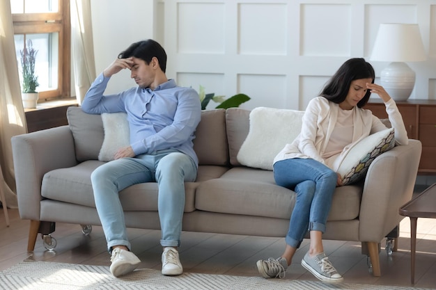 Unhappy young caucasian couple sit on sofa at home back to back think of breakup or divorce upset millennial man and woman have family fight disagreement struggle with relationships problems
