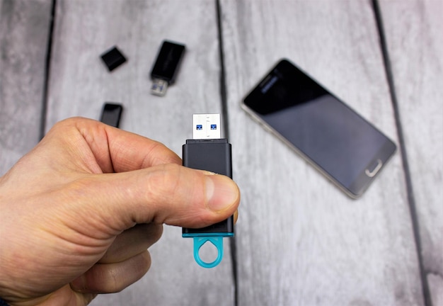 Unità flash USB in mano Supporto informazioni Un uomo detiene un disco USB sullo sfondo di un'unità flash e di un telefono