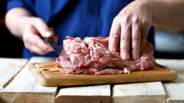 Uno chef con un coltello taglia un collo di maiale crudo. Carne di maiale cruda su un tagliere.