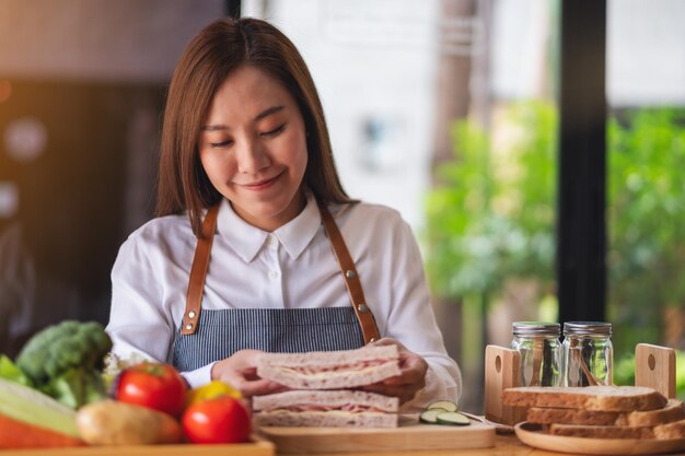 Uno chef femminile che cucina e tiene in mano un pezzo di panino al formaggio con prosciutto integrale in cucina