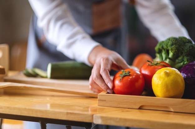 Uno chef femminile che tiene e raccoglie un pomodoro fresco da un vassoio di verdure sul tavolo