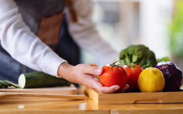 Uno chef femminile che tiene e raccoglie un pomodoro fresco da un vassoio di verdure sul tavolo