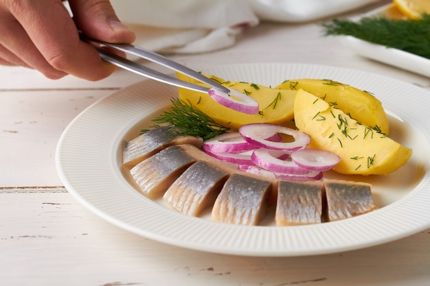Uno chef sta decorando un antipasto di filetto di aringa salato affettato con piatto bianco di patate e cipolla rossa