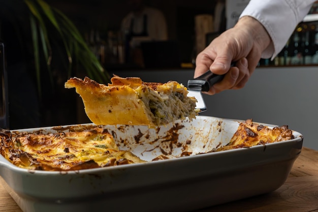 Uno chef sta tagliando una lasagna con una forchetta.