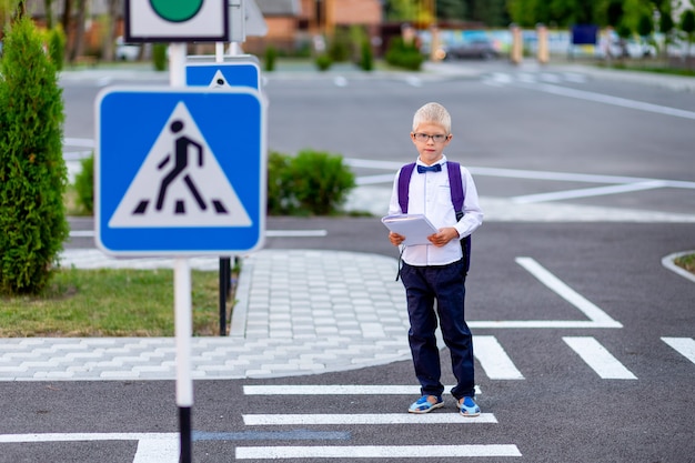 Uno scolaro biondo con gli occhiali e uno zaino va a scuola su un passaggio pedonale