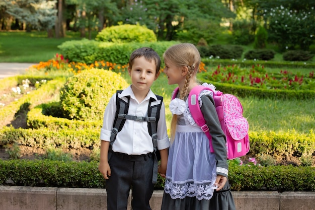uno scolaro con una camicia bianca con uno zaino e una ragazza bionda stanno parlando nel cortile della scuola
