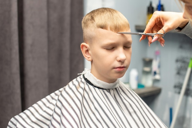 Uno scolaro è seduto in un negozio di barbiere che si fa i capelli con le forbici per tagliare i capelli