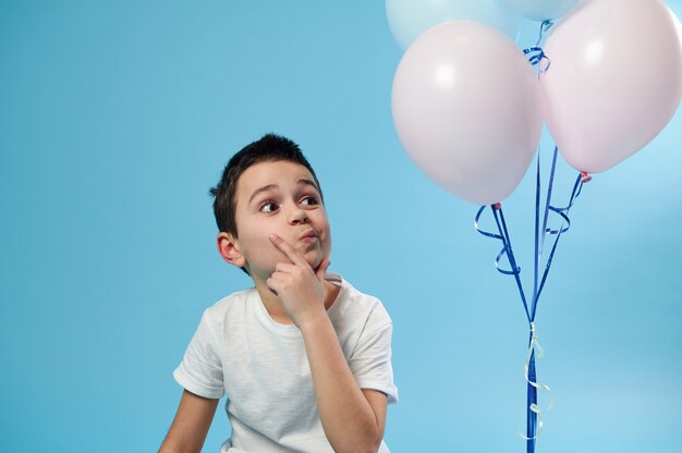 Uno scolaro in maglietta bianca guarda minuziosamente i palloncini sulla superficie blu