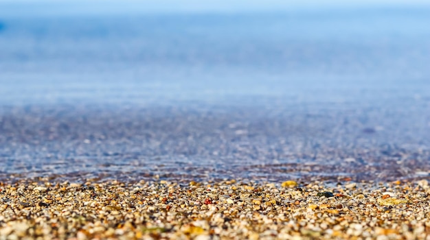 Uno sfondo di piccoli ciottoli di sabbia e onde che scorre sulla spiaggia del mare Concetto di vacanza estiva