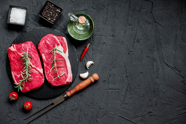Uno sfondo nero con due bistecche crude e un coltello con sopra l'aglio.