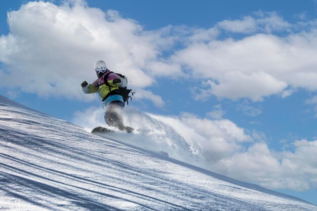 Uno snowboarder in maschera da sci e casco scende morbide colline di neve spargendo la neve