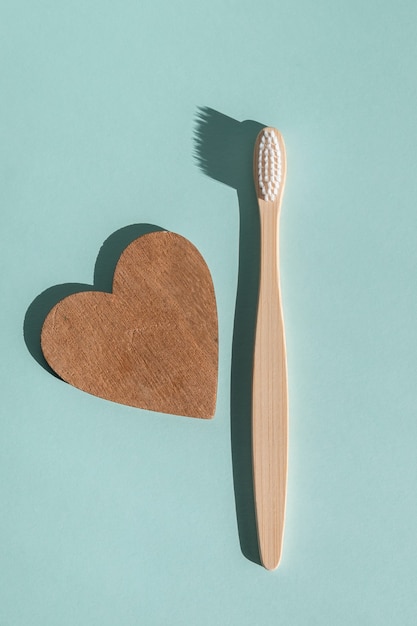 Uno spazzolino da denti in legno di bambù ecologico e un cuore di legno su uno sfondo azzurro