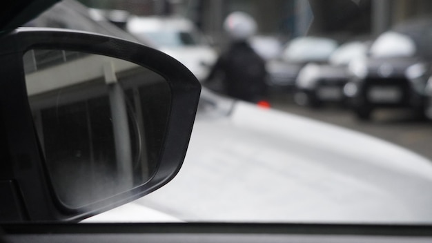 Uno specchietto laterale su un'auto mostra una persona con un casco e una motocicletta.