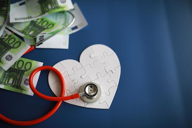 Uno stetoscopio sui soldi e un cuore puzzle Assicurazione sanitaria Sanità e medicina Quanto costa il trattamento Denaro e medicine Giornata mondiale del cuore Giornata mondiale della salute Quanto costa il cuore di un donatore