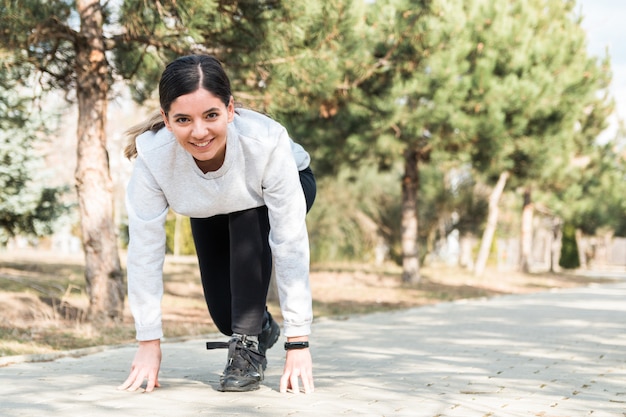 Uno stile di vita sano. donna attraente allegra pronta per iniziare a correre nel parco con alberi di pino al mattino