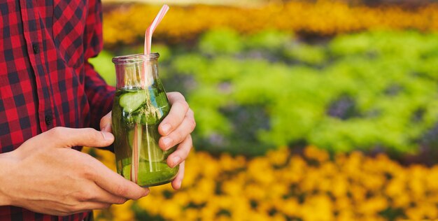 Uno stile di vita sano. Irriconoscibile giovane con cocktail detox in estate, su sfondo verde della natura.