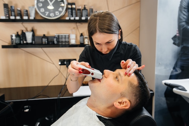 Uno stilista professionista in un barbiere moderno ed elegante rade e taglia i capelli di un giovane uomo. Salone di bellezza, parrucchiere.