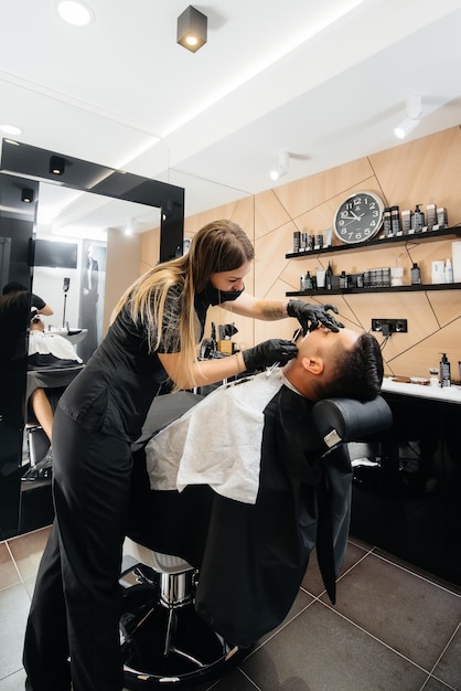 Uno stilista professionista in un moderno ed elegante barbiere rade e taglia i capelli di un giovane uomo