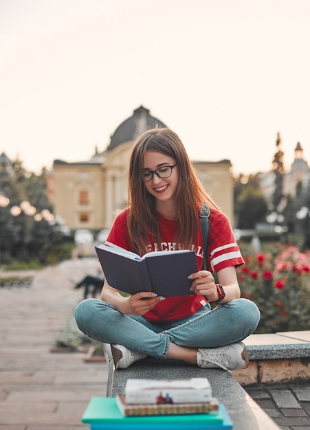 Uno studente con una maglietta rossa con uno zaino è seduto sul gradino, a gambe incrociate e legge un blocco note