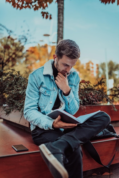 Uno studente seduto in un parco di fronte all'università e leggendo un libro