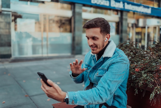 Uno studente vuoto seduto in un parco che utilizza uno smartphone e cuffie wireless