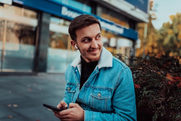 Uno studente vuoto seduto in un parco che utilizza uno smartphone e cuffie wireless