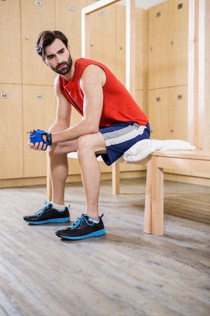 Unsmiling uomo seduto nello spogliatoio in palestra