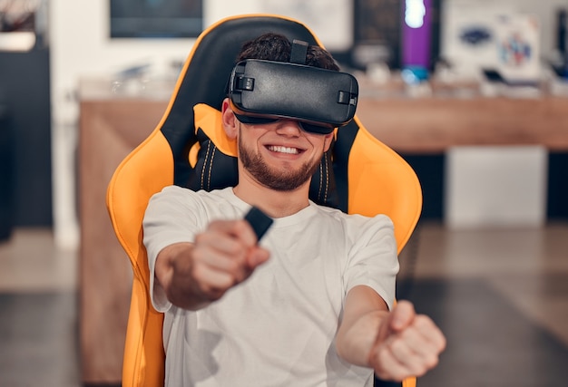 Uomini caucasici sorridenti in maglietta bianca che provano la tecnologia della realtà virtuale mentre sono seduti sulla sedia in un negozio di tecnologia.