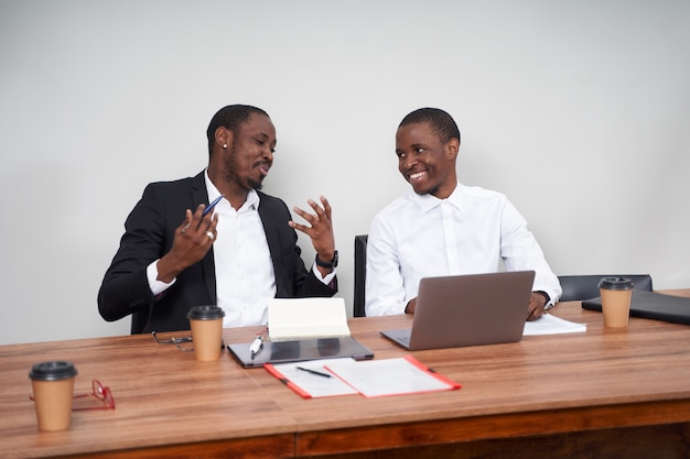 Uomini d'affari afroamericani di risata che discutono del lavoro di ufficio con un collega ad una tavola in un ufficio