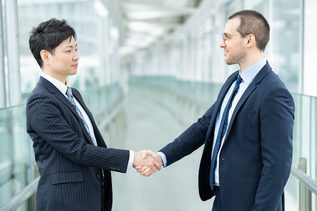 Uomini d'affari asiatici e caucasici si stringono la mano in giacca e cravatta