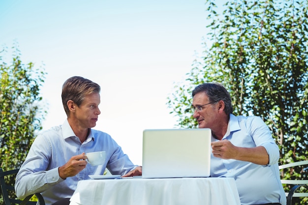 Uomini d'affari casuali che mangiano caffè e che per mezzo del computer portatile