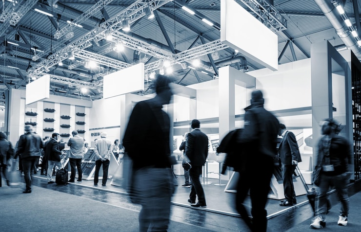 uomini d'affari che camminano allo stand di una fiera in una sala espositiva per eventi pubblici, con banner e spazio per la copia del testo individuale
