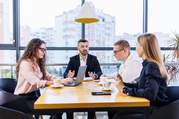 Uomini d'affari felici che guardano la presentazione del laptop, il successo sul lavoro, seduti in un ufficio moderno. Negoziazioni online di successo. Gli uomini d'affari condividono le loro conoscenze