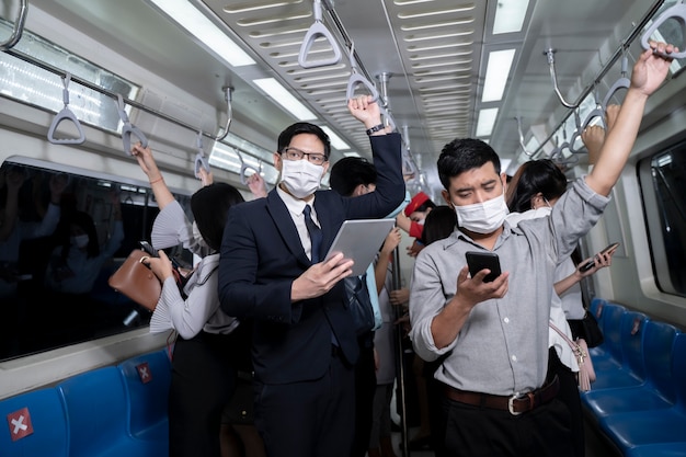 Uomini d'affari in piedi nella metropolitana di transito di massa della metropolitana. Uomo che utilizza tablet e smartphone. persone che indossano la maschera per il viso. Virus influenzale del coronavirus nei viaggi pubblici.