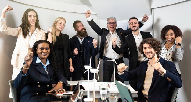 Uomini d'affari multietnici gioiosi che guardano la fotocamera all'interno dell'ufficio aziendale per una foto di gruppo mentre lavorano insieme su un progetto di innovazione sostenibile Concetto di raggiungimento degli obiettivi