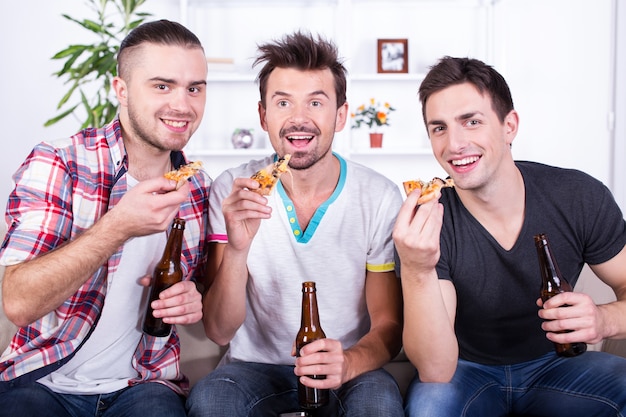 Uomini eccitati guardano il calcio con birra e pizza.