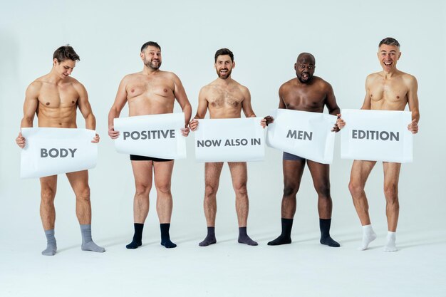 Uomini multietnici che posano per un set di bellezza positivo per il corpo in edizione maschile che mostra messaggi sui banner. Ragazzi a torso nudo con età diverse e un corpo che indossa biancheria intima da boxer