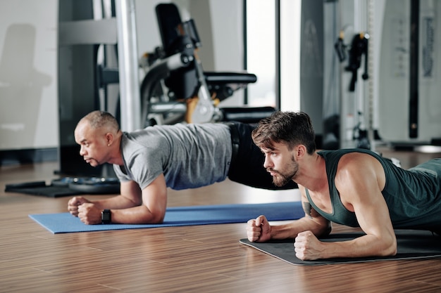 Uomini seri e concentrati in piedi in posizione di plancia sul pavimento della palestra