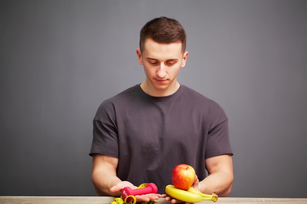 Uomo a forma di corpo sano che tiene una frutta fresca e cibo spazzatura.