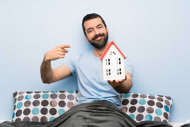 Uomo a letto con la barba che tiene una casetta