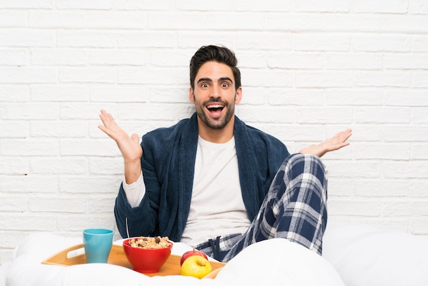 Uomo a letto con la vestaglia e fare colazione con espressione facciale scioccata