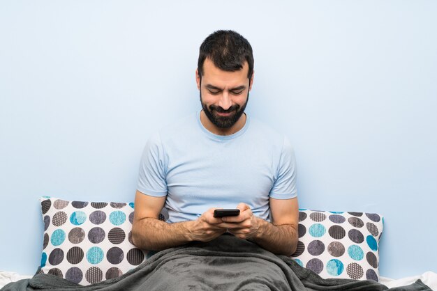 Uomo a letto inviando un messaggio con il cellulare