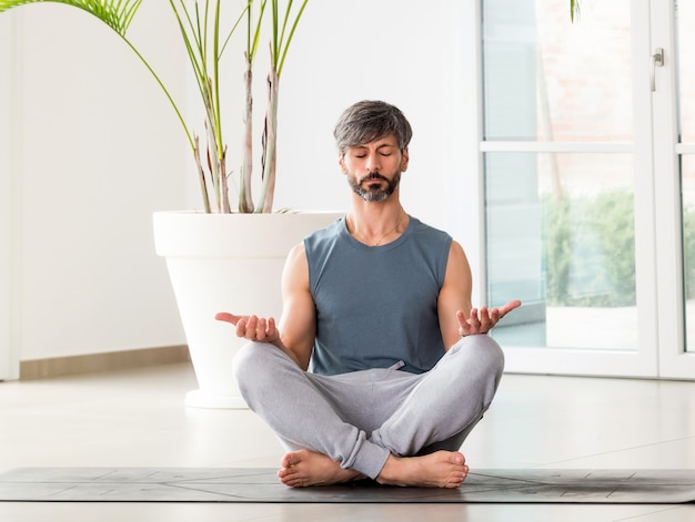 Uomo a piedi nudi che medita nella posa Padmasana o Lotus con un'espressione serena sul pavimento di una stanza ad alta chiave con copyspace in un concetto di benessere, salute e rilassamento mentale