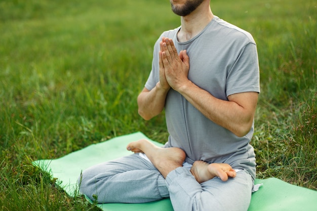 Uomo a praticare yoga sull'erba verde del parco