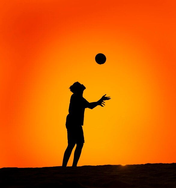 Uomo a silhouette che gioca a calcio contro un cielo arancione limpido